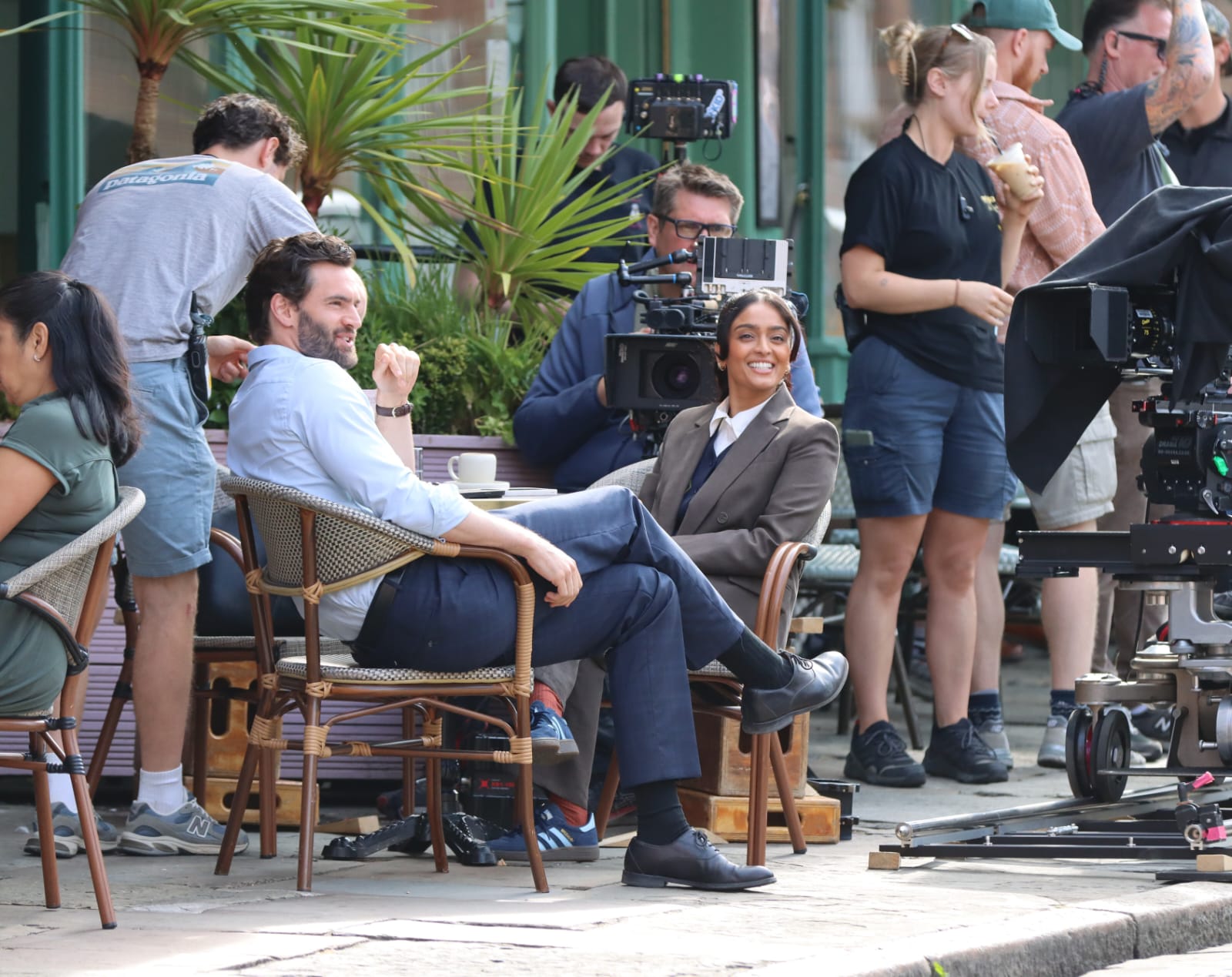 Filming for Netflix’s upcoming thriller The Woods has continued in Liverpool, with two of the show’s leading actors spotted in the city’s Georgian Quarter. Tom Bateman and Mandeep Dhillon were seen filming scenes outside Papillon and The Quarter on Tuesday 21 July, as production crews returned to Liverpool for the latest shoot. Explore Liverpool’s photographer captured a new collection of images from the set as filming took place around the corner of Hope Street and Falkner Street. Papillon is located on Hope Street, with its outdoor area wrapping around the corner onto Falkner Street, while neighbouring restaurant The Quarter sits just a short distance away. Bateman was once again seen in character as leading barrister Paul ‘Cope’ Copeland, alongside Mandeep Dhillon, who plays Loren Muse in the eight-part Netflix series. Details surrounding the scenes remain under wraps, but the latest photographs show the pair together outside the popular Georgian Quarter venues. The latest shoot gives viewers another glimpse behind the scenes as the production continues to use recognisable locations across Liverpool and the wider North West. Filming has previously taken place at St George’s Hall, where Bateman was photographed shooting scenes that appeared to show his character leaving court. The production has also used Hamilton Square in Birkenhead as one of its locations. What is Netflix’s The Woods about? Based on Harlan Coben’s 2007 novel, The Woods follows Paul ‘Cope’ Copeland, whose sister Camille disappeared from a summer camp 20 years earlier. Now a successful barrister and single father, Cope has attempted to rebuild his life following the tragedy. However, the discovery of the body of a man believed to have died alongside Camille leads him to question whether his sister may also have survived. His search for answers uncovers years of secrets, lies and cover-ups that threaten the life he has created. Mandeep Dhillon stars as Loren Muse, while Michelle Keegan plays Cope’s former love, Lucy Silverfield. The cast also includes Pearce Quigley, James Buckley, Tracy-Ann Oberman, Roger Barclay and Charlotte Beaumont. The limited series has been written by Danny Brocklehurst, whose previous Harlan Coben adaptations for Netflix include Fool Me Once, Stay Close and Run Away. Production is taking place in partnership with Manchester-based Quay Street Productions, with filming continuing at locations across the North West. Netflix has not yet confirmed a release date for The Woods.